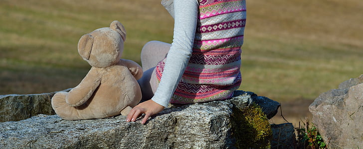 person sitting beside brown bear plush toy during daytime