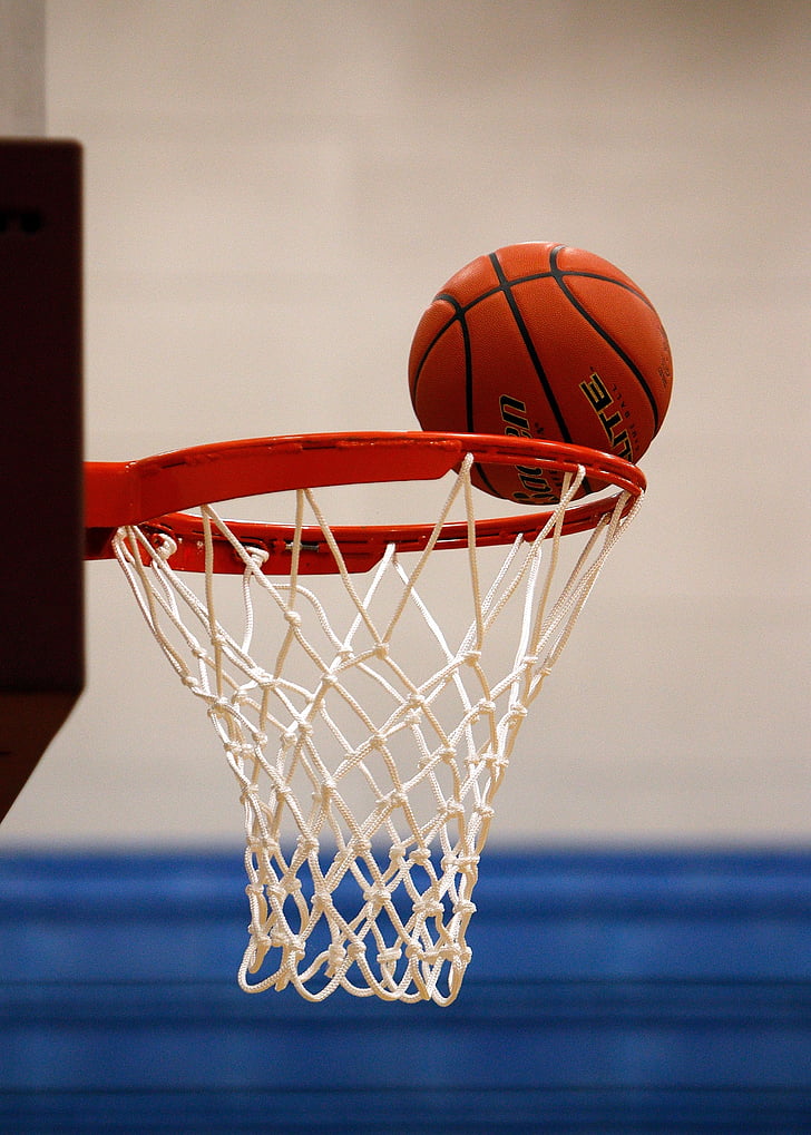 brown basketball on edge of white and red basketball hoop