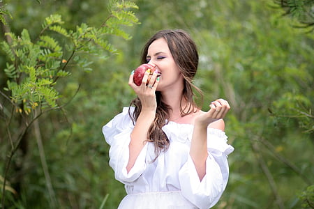 woman in white off-shoulder dress holding red apple