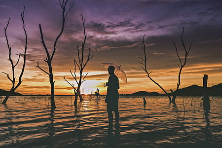 silhouette of man holding umbrella on body of water