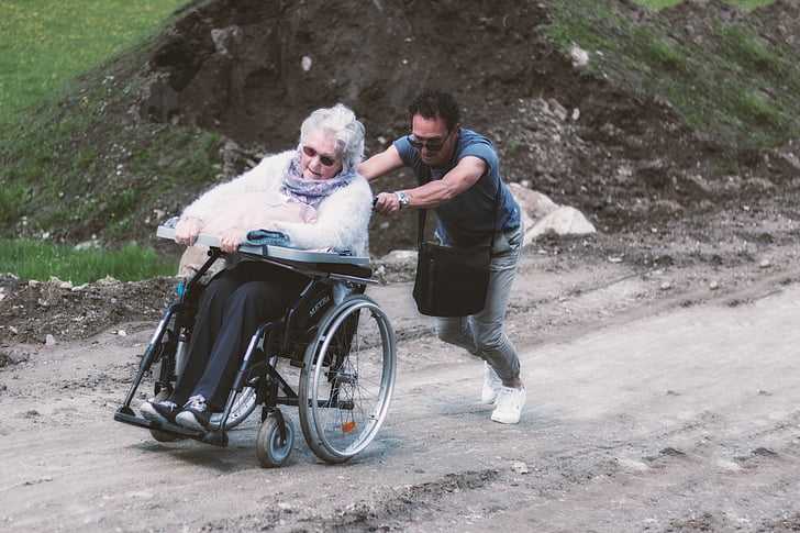 man pushing adult woman's wheelchair during daytime