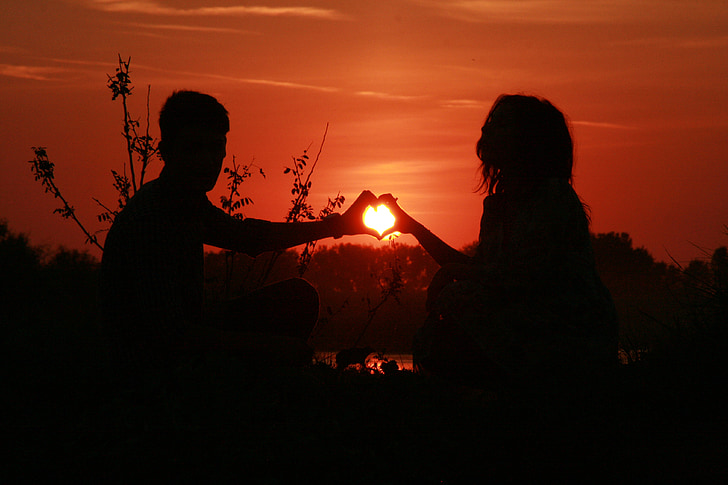 silhouette of two person making heart hand sign