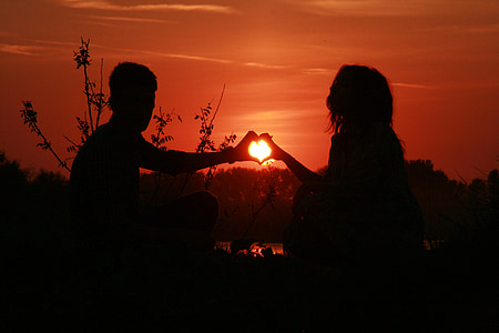 silhouette of two person making heart hand sign