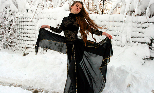 woman wearing black abaya dress opening her dress wide standing near fence covered with snow during daytime
