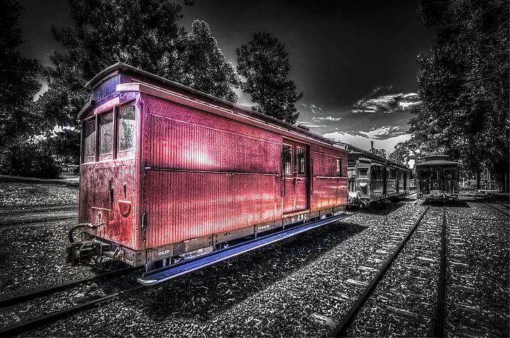 selective color photography of train under cloudy sky