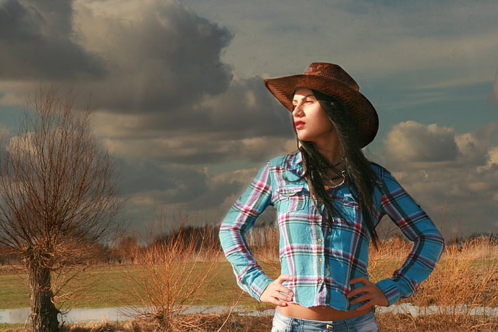 woman in blue and red sport shirt and brown cowboy hat near green sand