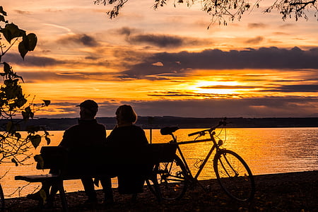 silhouette of man and woman sitting on bench facing body of water