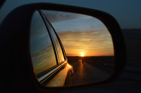 vehicle side mirror showing following vehicle on road during sunset