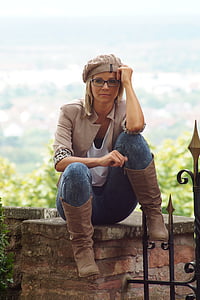 sitting woman wearing knit cap, white shirt, beige blazer, blue denim pants, and brown leather boots
