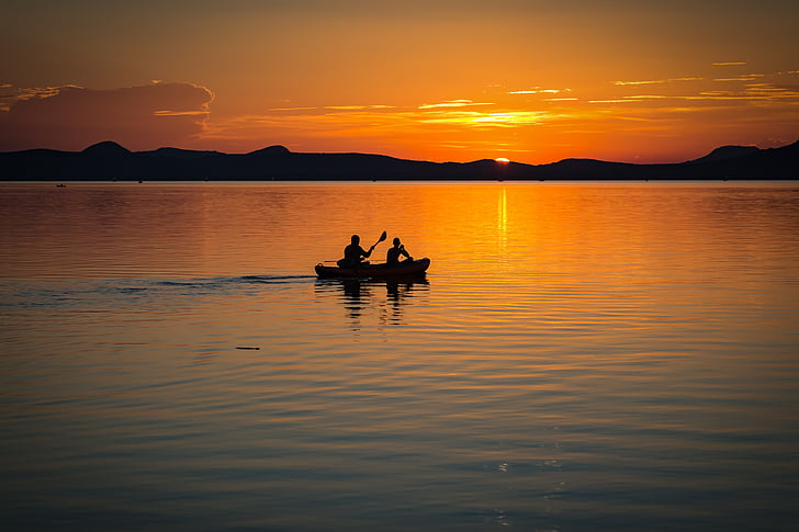 silhouette photography of two person on boat sailing during golden hour