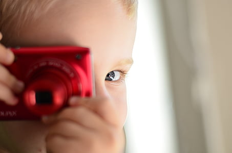 selective focus photography of boy holding red compact camera