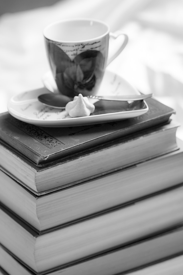 greyscale photo of teacup on top book stack