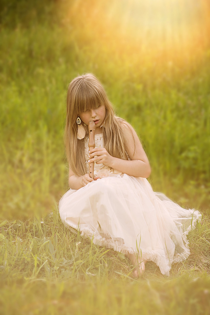 girl sitting on grass while playing wooden flute