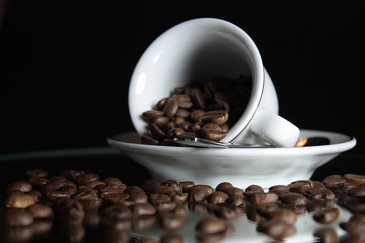 selective focus photo of white ceramic teacup on saucer with coffee beans