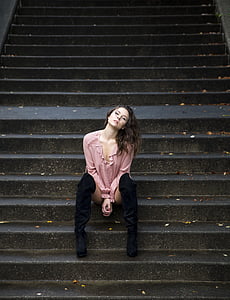woman wearing pink long-sleeved shirt sitting on black concrete stairs