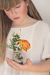 woman holding clear glass jar with orange and red ranunculus flower