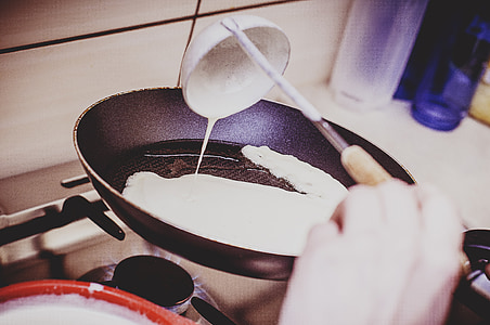 person holding pouring white cream using ladle on frying pan on stove