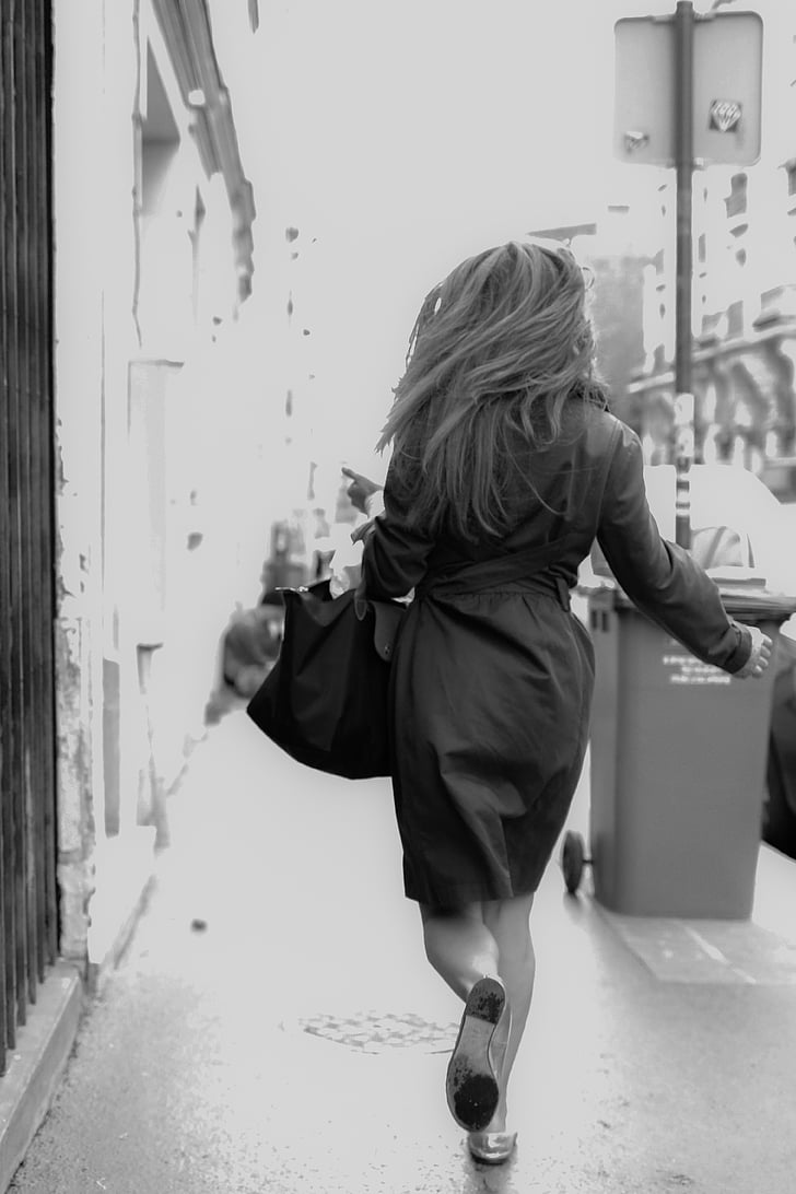 greyscale photography of woman walking on sidewalk