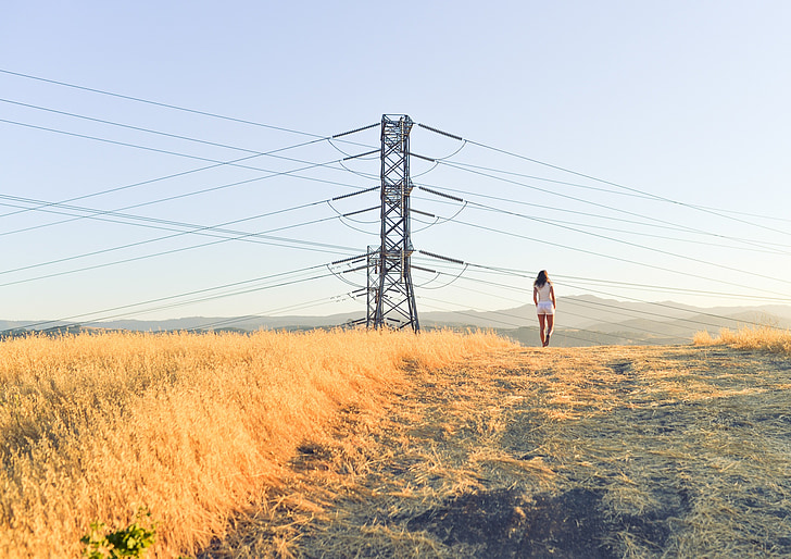 person standing on grass field near electricity post