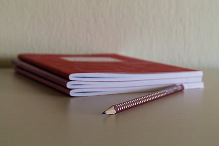 red and beige pencil beside three red notebooks