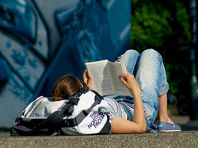 man lying on pavement reading books