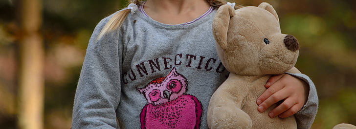 selective focus photography of girl holding bear plush toyt