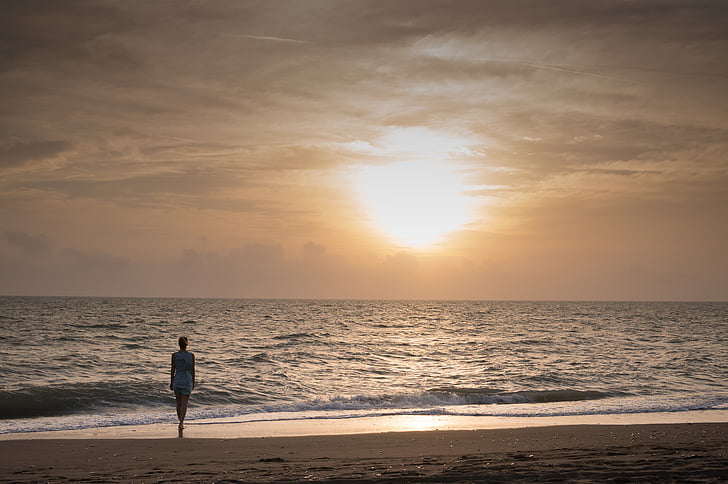 woman walking on shoreline during golden hour