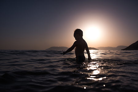 silhouette of a child on water against sunset