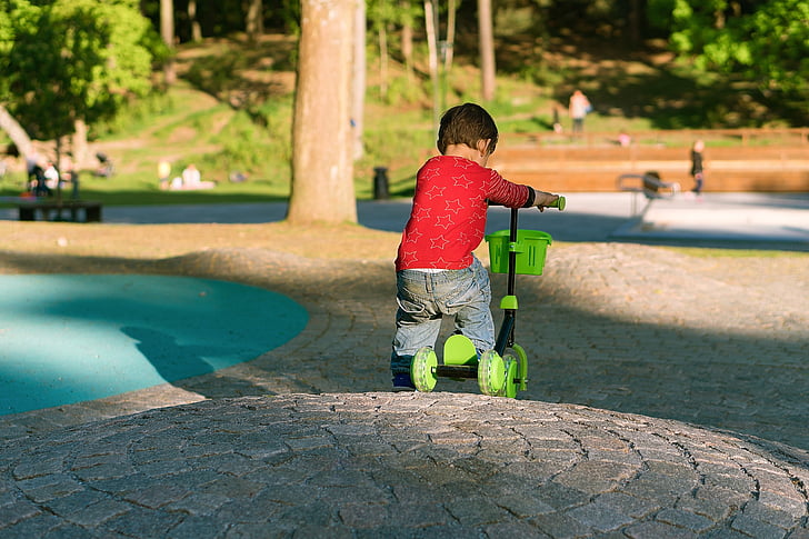 boy wearing red long-sleeved shirt riding black and green tri kick scooter