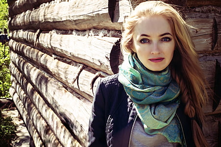 woman wearing black jacket and green scarf standing behind wood fence