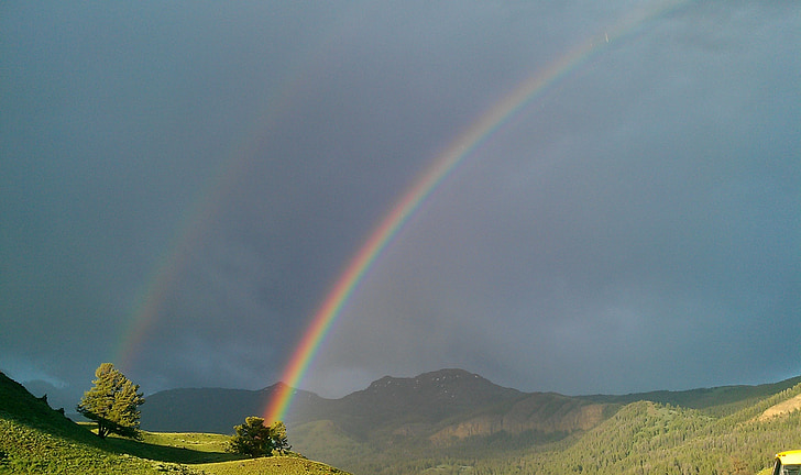 green mountain and trees with rainbow during daytime