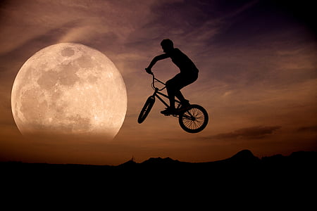 silhouette of man riding bicycle on mid air during sunset