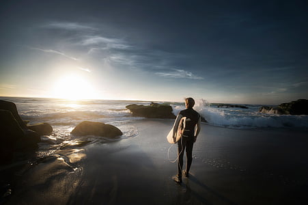 surfer looking at sunset on beach shore