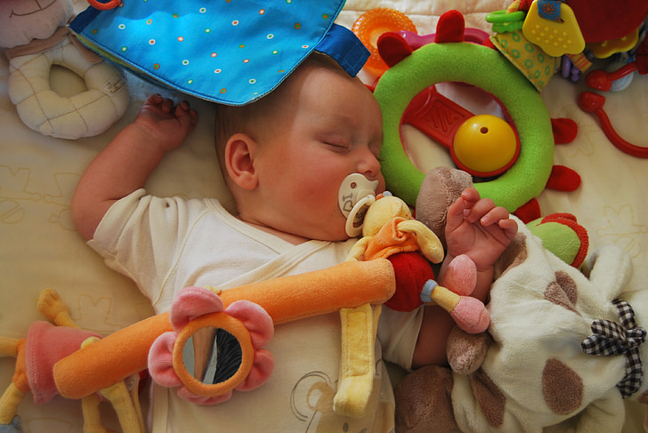 baby sleeping on white fabric sheet surrounded by toys