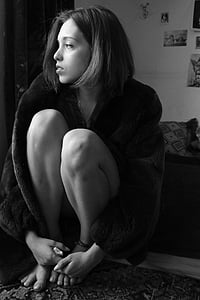 grayscale photo of woman wearing coat sitting with knees to chest