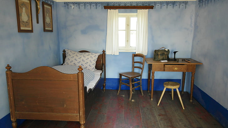 brown wooden bed and white mattress near table and window