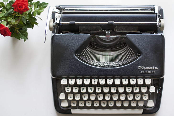 aerial view photography of black typewriter beside red roses