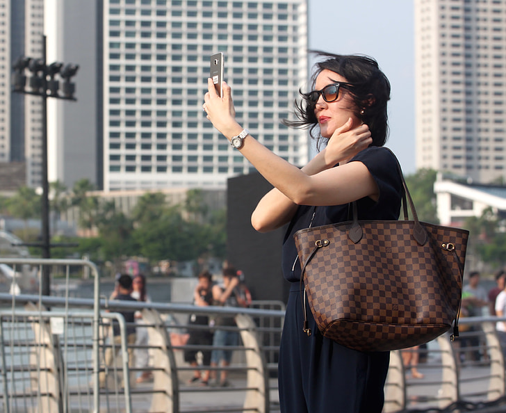 woman wearing tote bag holding silver-colored smartphone