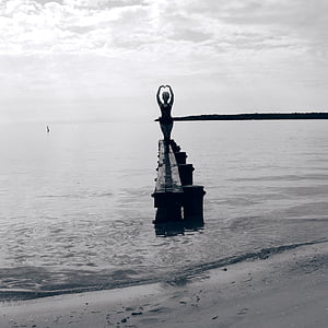 grayscale photo of woman standing on rock formation on sea