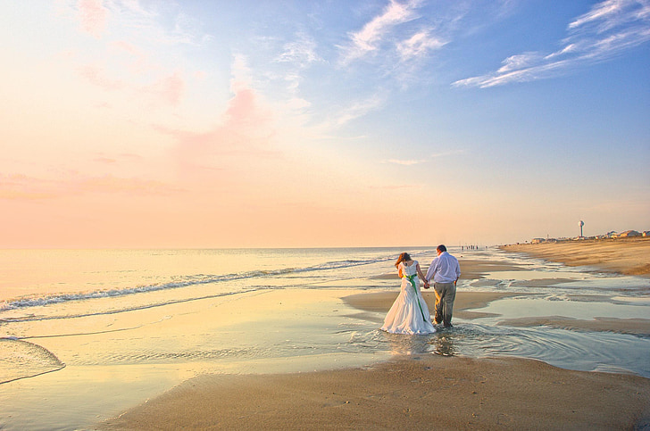 couple holding hands on shore near sea