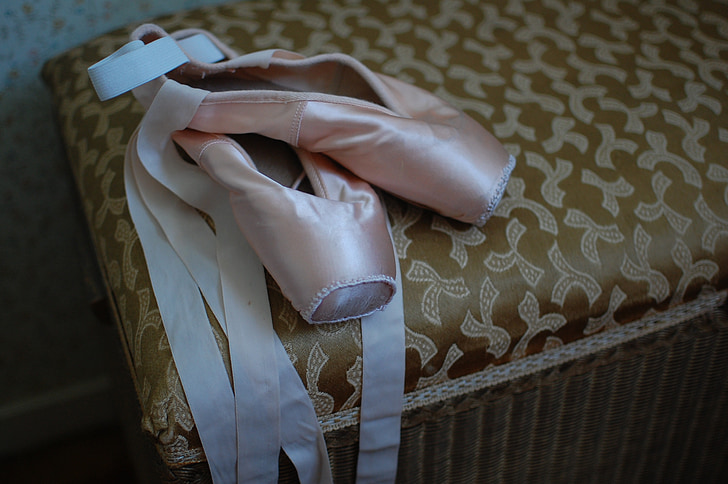 pair of pink ballet shoes on brown fabric ottoman