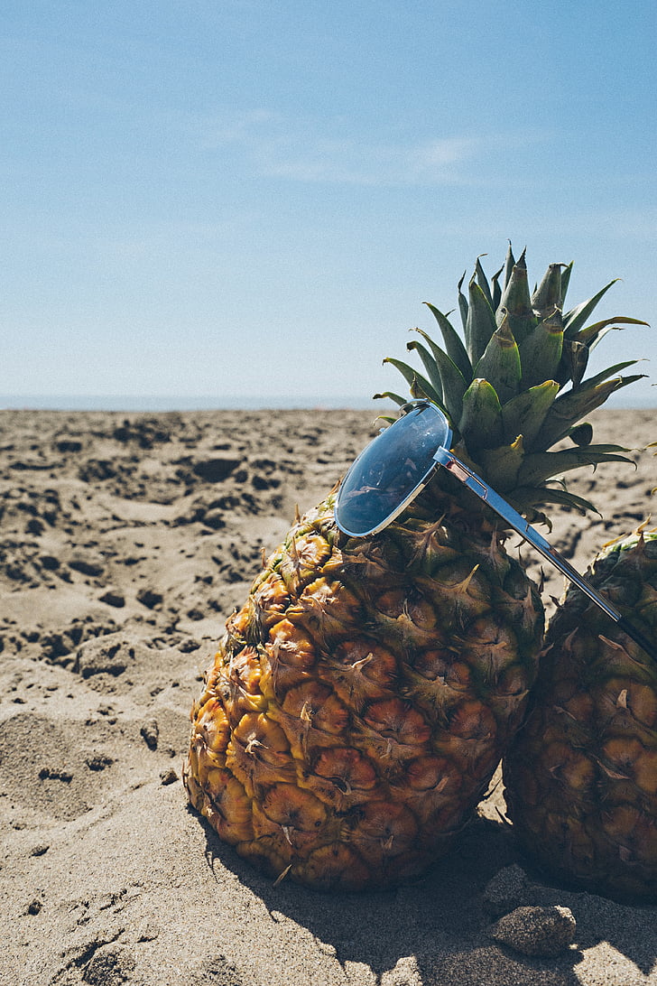 sunglasses and pineapple on white sand