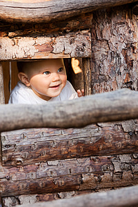 baby in whit v-neck shirt peeping through brown wooden windpw