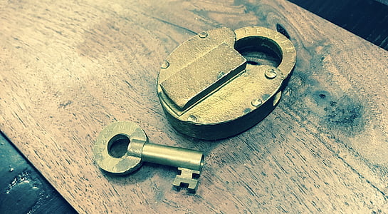 gray padlock beside key on brown wooden board