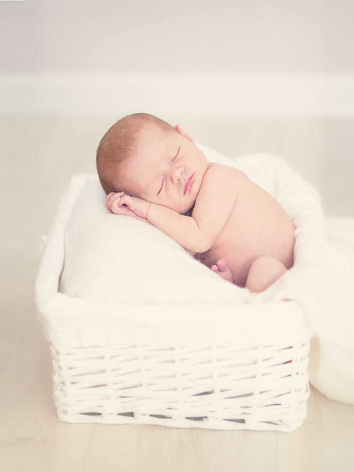 sleeping baby lying on white pillow on white wicker basket