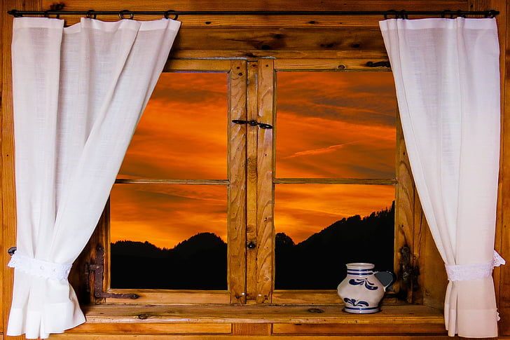 brown wooden window with two curtains and view of orange sunset