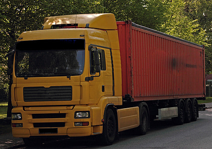 yellow and red container truck packed under trees