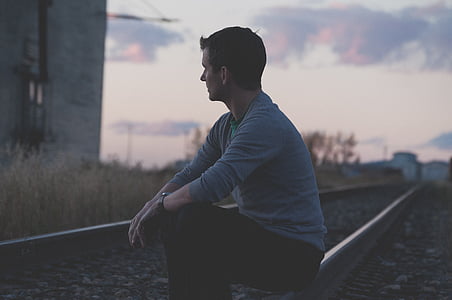 man wearing gray long-sleeved shirt sitting on train rail