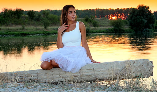 woman wears white sleeveless dress near river during sunset