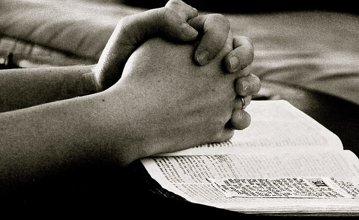 person praying hands on boook